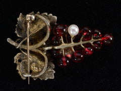 thumbnail of Reverse side of antique French brooch with enameled green grape leaves and a cluster of red glass and pearl grapes. Shown on black background.
