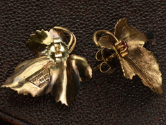 thumbnail of Back of a pair of grape leaf shaped earrings in 18K yellow gold with ruby centers, shown on dark background. Stamps on the back read "Tiffany & Co 18KT Italy" and "18K" on the earring back. 