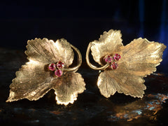 thumbnail of Pair of grape leaf shaped earrings in 18K yellow gold with ruby centers, shown on dark background.