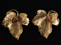 thumbnail of Pair of grape leaf shaped earrings in 18K yellow gold with ruby centers, shown with leaf tips pointed down on dark background.