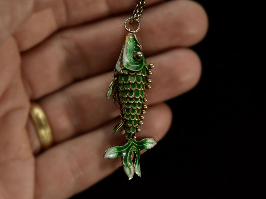 Hand holding a c1960 Green Enamel Fish Pendant 