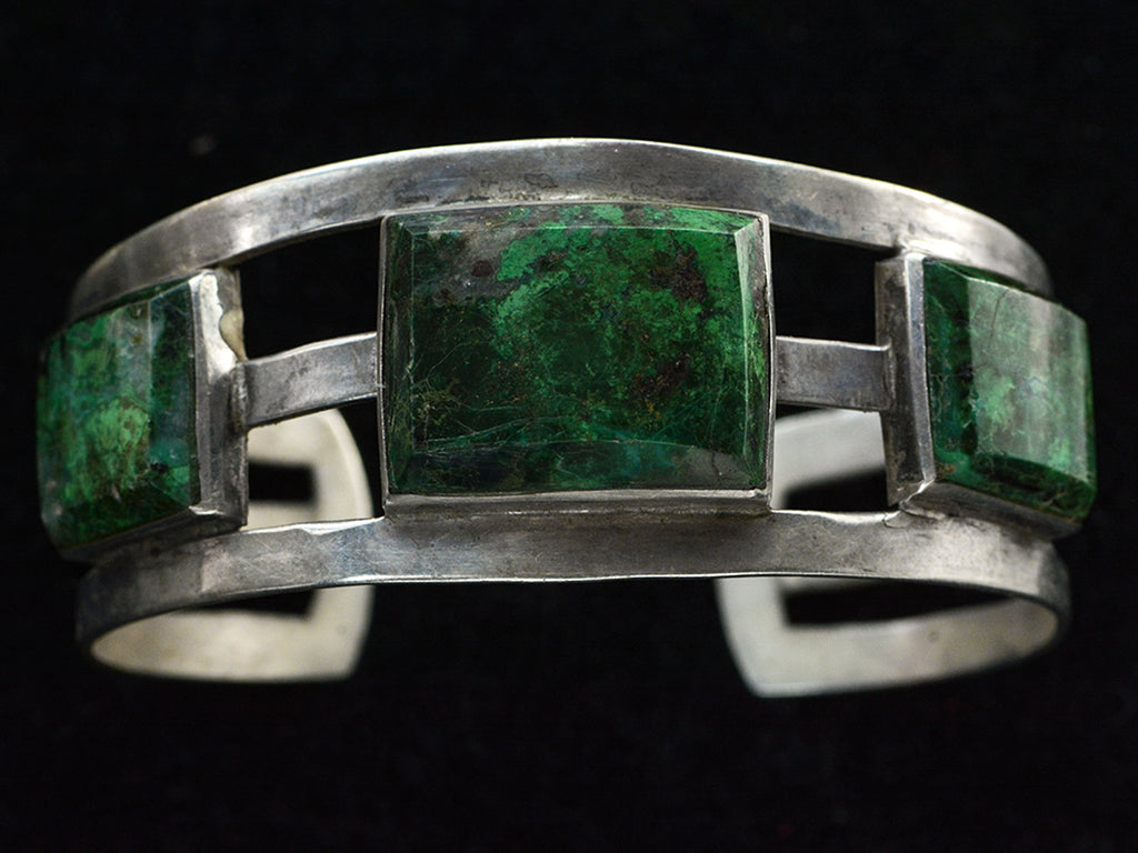 A sterling silver cuff bracelet featuring three rectangular green stone inlays with natural matrix patterns, set against a solid black background.