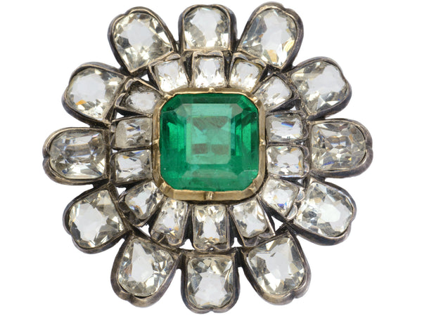 A 19th century silver and gold brooch with a green crystal surrounded by petals of clear white faceted crystals, shown on white background.