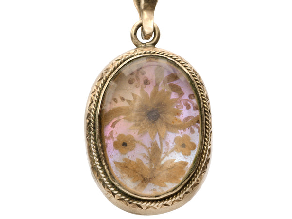 Victorian gold mourning pendant with blond hair arrange in a floral design on iridescent mother of pearl, shown on white background.