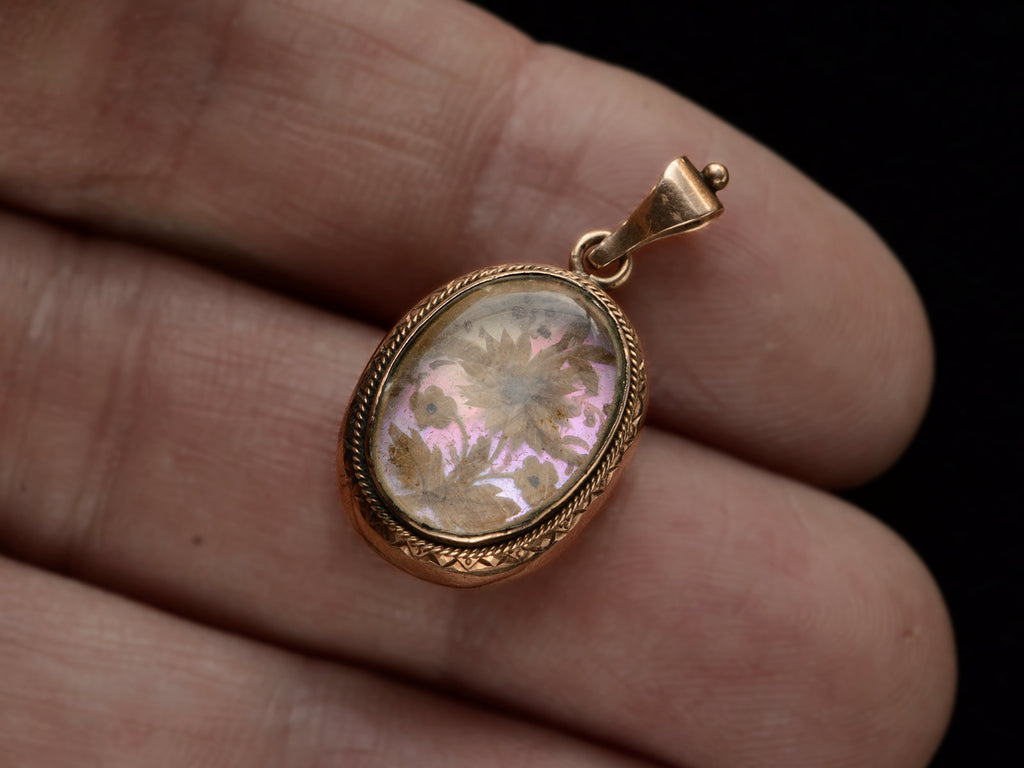 Victorian gold mourning pendant with blond hair arrange in a floral design on iridescent mother of pearl, shown on hand.