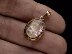 thumbnail of Victorian gold mourning pendant with blond hair arrange in a floral design on iridescent mother of pearl, shown on hand.