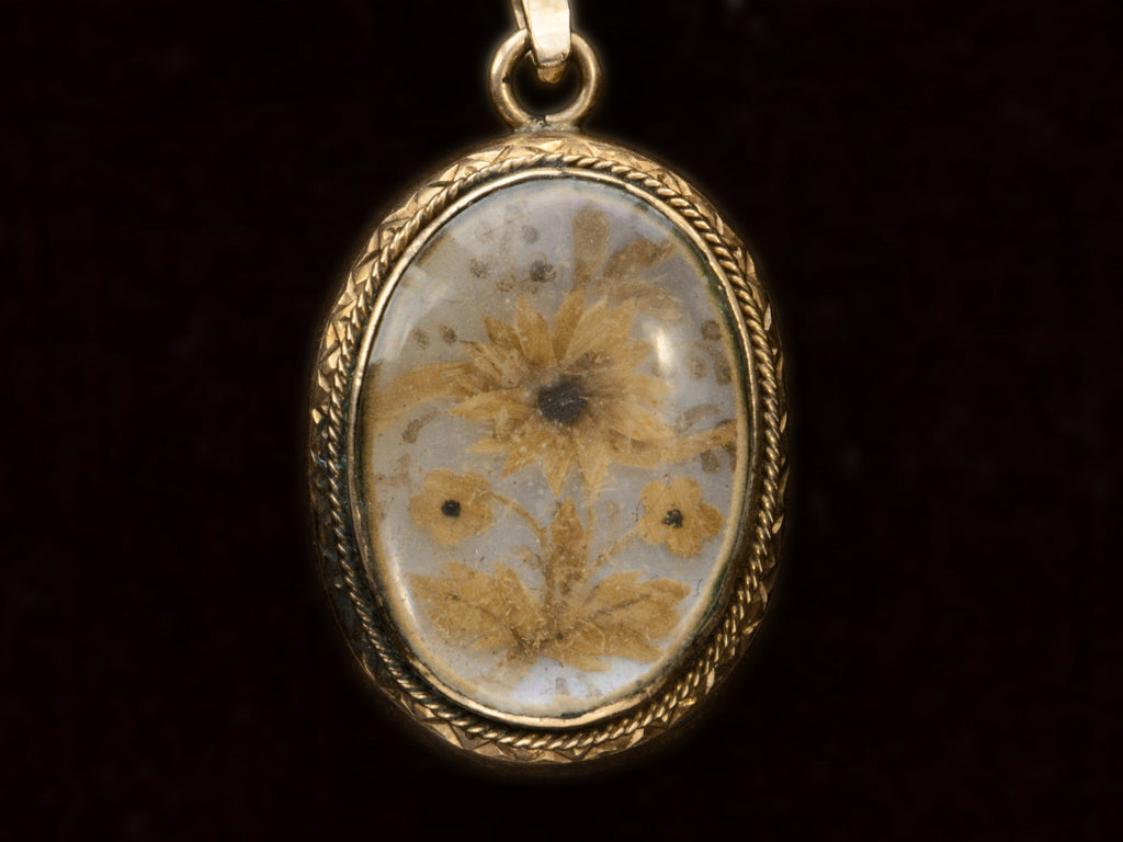 Victorian gold mourning pendant with blond hair arrange in a floral design on iridescent mother of pearl, shown on black background.