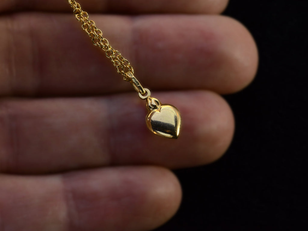 Yellow gold flaming heart shaped charm  hanging on a cable chain, shown held in hand.  A stamp on the bale reads "750."