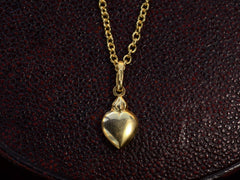 thumbnail of Yellow gold flaming heart shaped charm  hanging on a cable chain, shown on dark textured background.  A stamp on the bale reads "750."