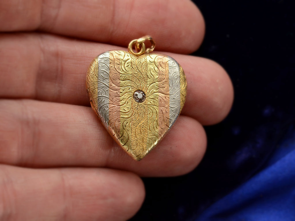 c1900 Heart Locket in yellow gold with stripes of platinum and rose gold and a pink diamond center, shown on hand for scale