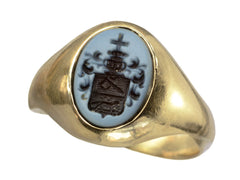 thumbnail of An antique yellow gold signet ring with an oval black and blue chalcedony intaglio with an armorial coat of arms (a cross on top of a crown on top of a shield with an axe and a fox), shown on white background.