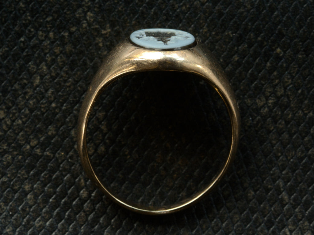 Side profile of an antique yellow gold signet ring with an oval black and blue chalcedony intaglio shown on dark textured background.