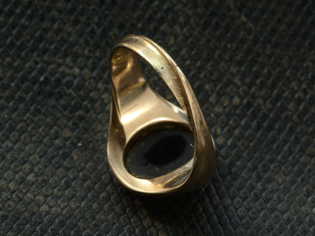 Reverse view of antique yellow gold signet ring, showing a twisted shank, shown on dark textured background.