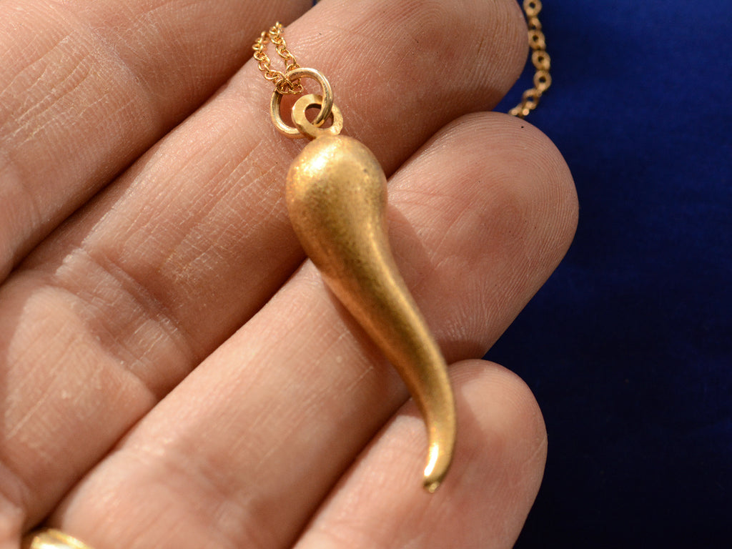 Vintage Italian cornicello horn charm in yellow gold, on hand for scale.