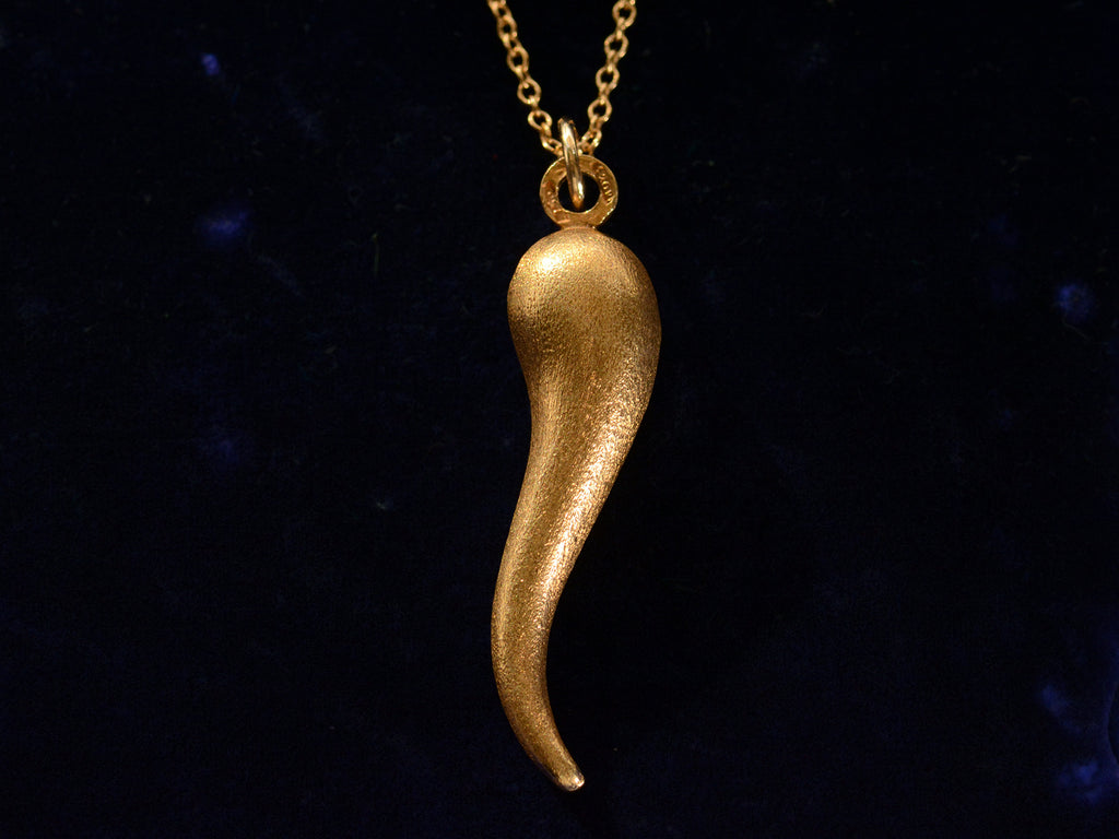 Vintage Italian cornicello horn charm in yellow gold, on dark blue background.