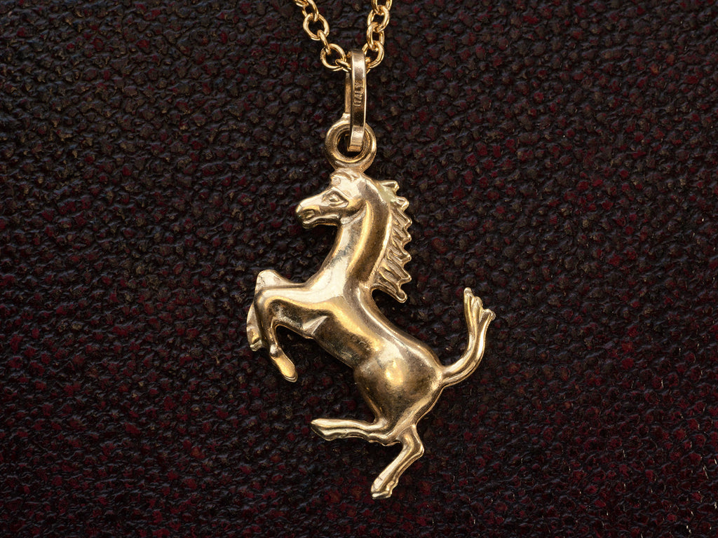Gold horse pendant necklace on a dark textured background. "ITALY" stamp visible on bale.
