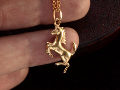 thumbnail of Gold horse-shaped pendant on a chain held between fingers against a dark background