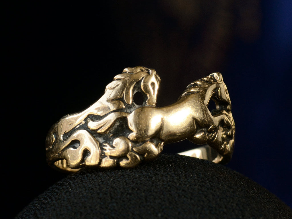 Vintage gold ring with pair of running horses, shown on dark background.