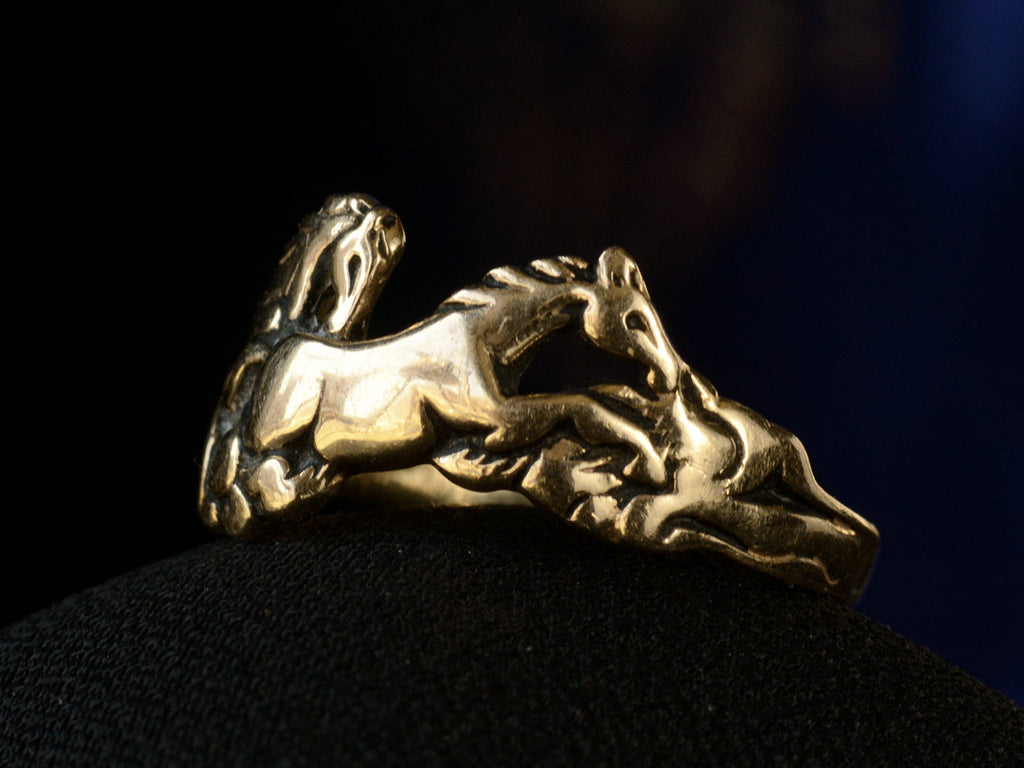 Right angled view of vintage gold ring with pair of running horses, shown on dark background.