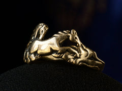 thumbnail of Right angled view of vintage gold ring with pair of running horses, shown on dark background.