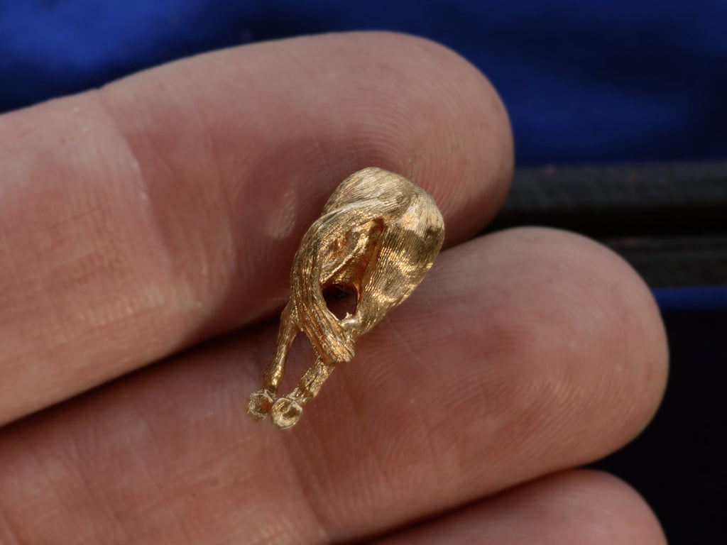 A vintage yellow gold tie tack in the form of a horse's ass. Shown on a hand for scale.