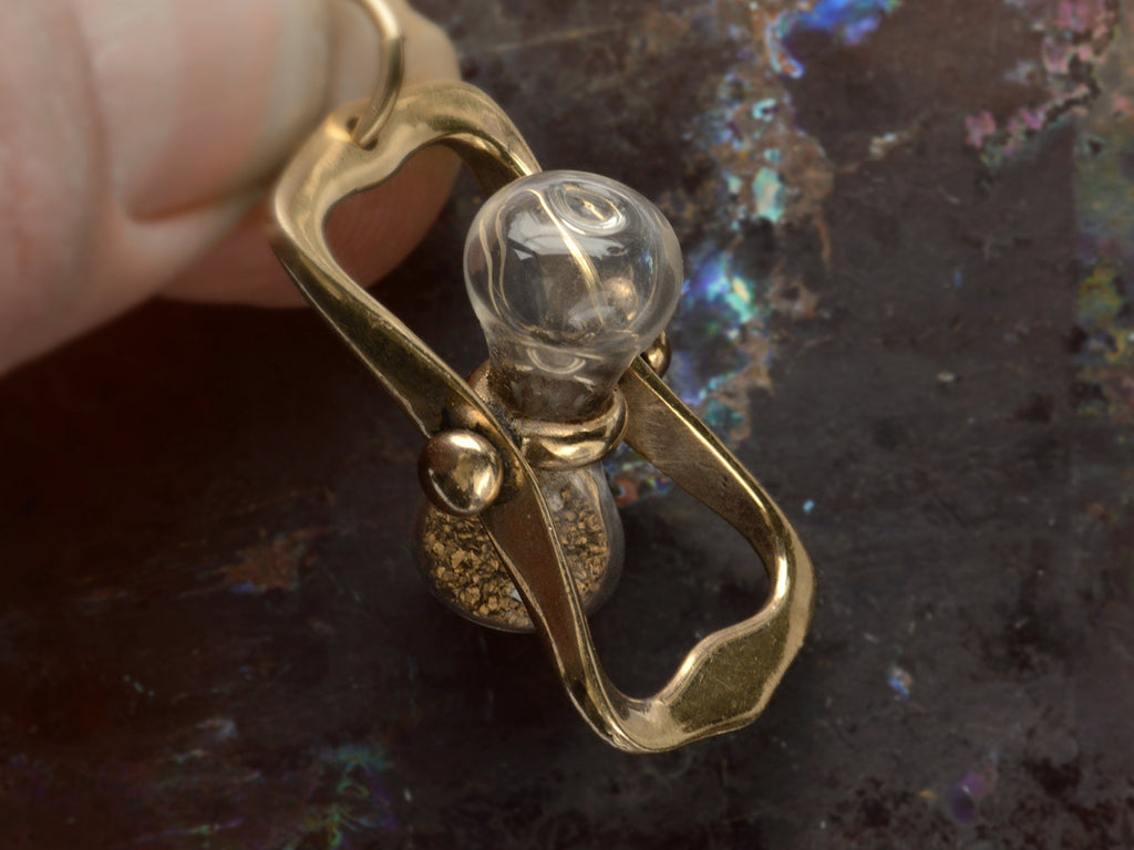 c1970 Yellow Gold Hourglass Pendant with Gold Flakes inside glass (showing how the glass rotates). Held in fingers.
