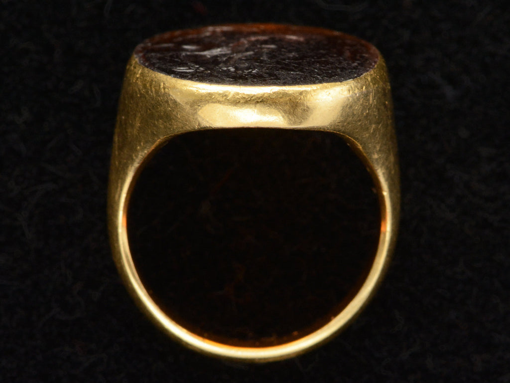 Side profile of antique yellow gold signet ring with amber glass intaglio of classical scene (Eros fishing), shown on dark background.