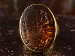 thumbnail of Face profile view of antique yellow gold signet ring with amber glass intaglio of classical scene (Eros fishing), shown on dark background.
