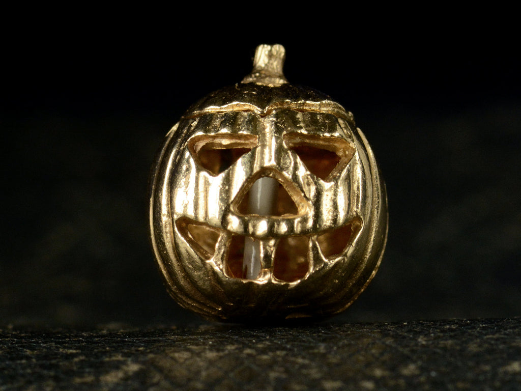 Front view of vintage gold Jack-O'-Lantern charm, on dark background.