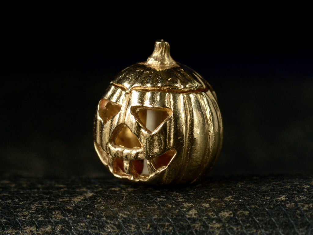 Angled front view of vintage gold Jack-O'-Lantern charm, on dark background.