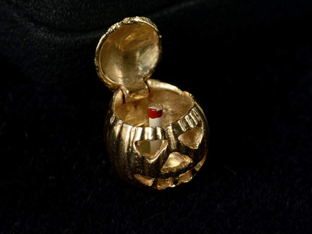 A vintage gold Jack-O'-Lantern charm, on dark background, shown with lid open shown red and white candle inside. On dark background.
