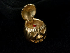 thumbnail of A vintage gold Jack-O'-Lantern charm, on dark background, shown with lid open shown red and white candle inside. On dark background.