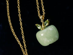 thumbnail of Detail view of light green apple shaped pendant carved from jade with a gold stem and peridot leaves, shown with cable chain on black background.
