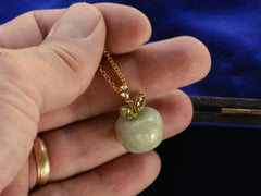 thumbnail of Hand holding a light green apple shaped pendant carved from jade with a gold stem and peridot leaves.