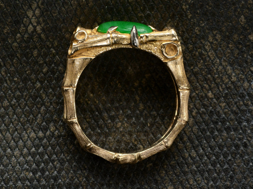 Side profile view of a vintage gold jade and diamond ring with a mounting designed to look like bamboo, shown on dark textured background.