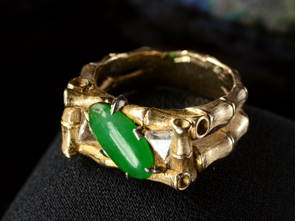 Elevated right angled view of a vintage gold jade and diamond ring with a mounting designed to look like bamboo, shown on dark background.
