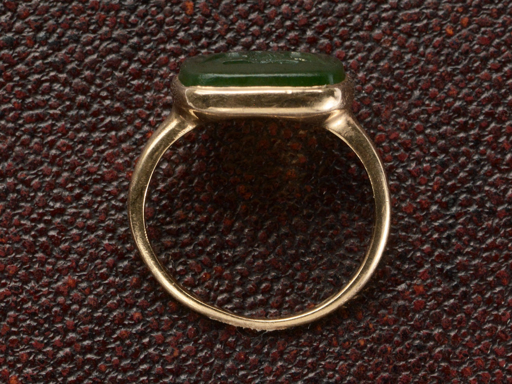 Side profile of an antique signet ring with a dark green intaglio mounted in rosy-yellow gold and shown on dark textured background.