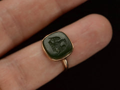 thumbnail of An antique signet ring with a dark green intaglio carved with the image of a crane stretching his wings over a crown, mounted in rosy-yellow gold and shown on finger