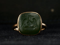 thumbnail of An antique signet ring with a dark green intaglio carved with the image of a crane stretching his wings over a crown, mounted in rosy-yellow gold and shown on dark background.