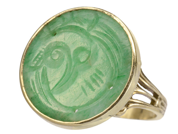 A c1930 yellow gold ring with a round flat jade carving mounted in a bezel, shown on white background.