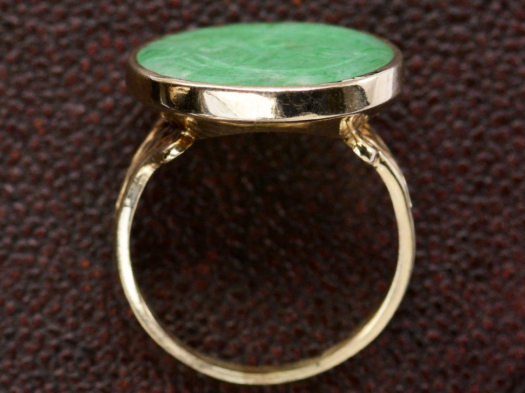 Side profile view of back of antique jade and yellow gold ring, shown on textured background.