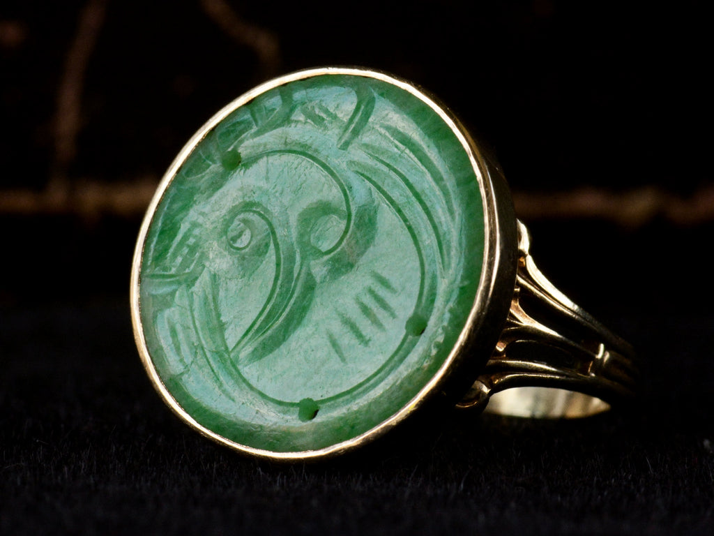 Right angled view of c1930 yellow gold ring with a round flat jade carving mounted in a bezel, shown on dark background.