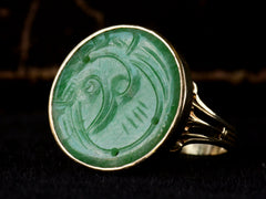 thumbnail of Right angled view of c1930 yellow gold ring with a round flat jade carving mounted in a bezel, shown on dark background.