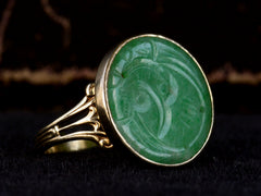 thumbnail of Left angled view of c1930 yellow gold ring with a round flat jade carving mounted in a bezel, shown on dark background.