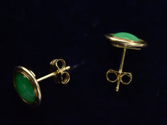 thumbnail of Side view of a pair of green jade cabochon stud earrings with 14k yellow gold frames, shown on dark background.