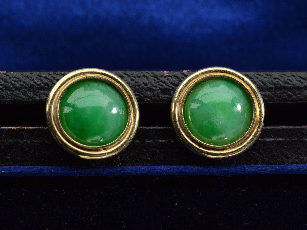 Front view of a pair of green jade cabochon stud earrings with 14k yellow gold frames, shown on dark background.