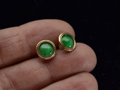 thumbnail of A pair of green jade cabochon stud earrings with 14k yellow gold frames, shown on held in between fingers.