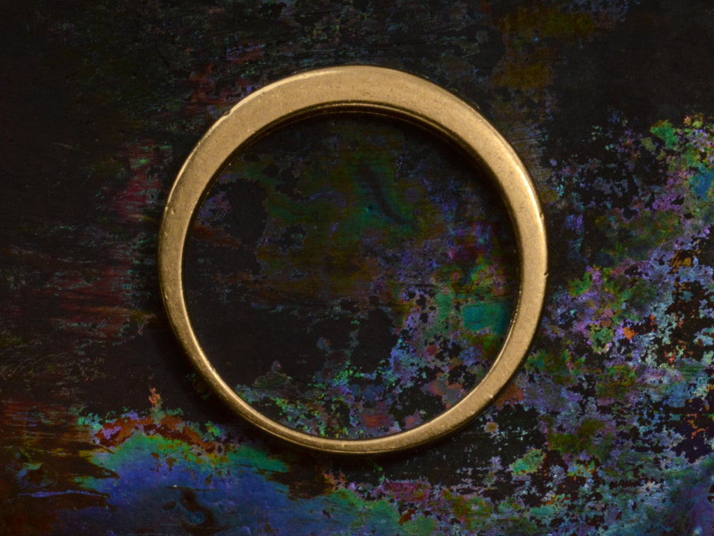 Side profile a diamond band showing flat yellow gold edges, on a dark colorful background.