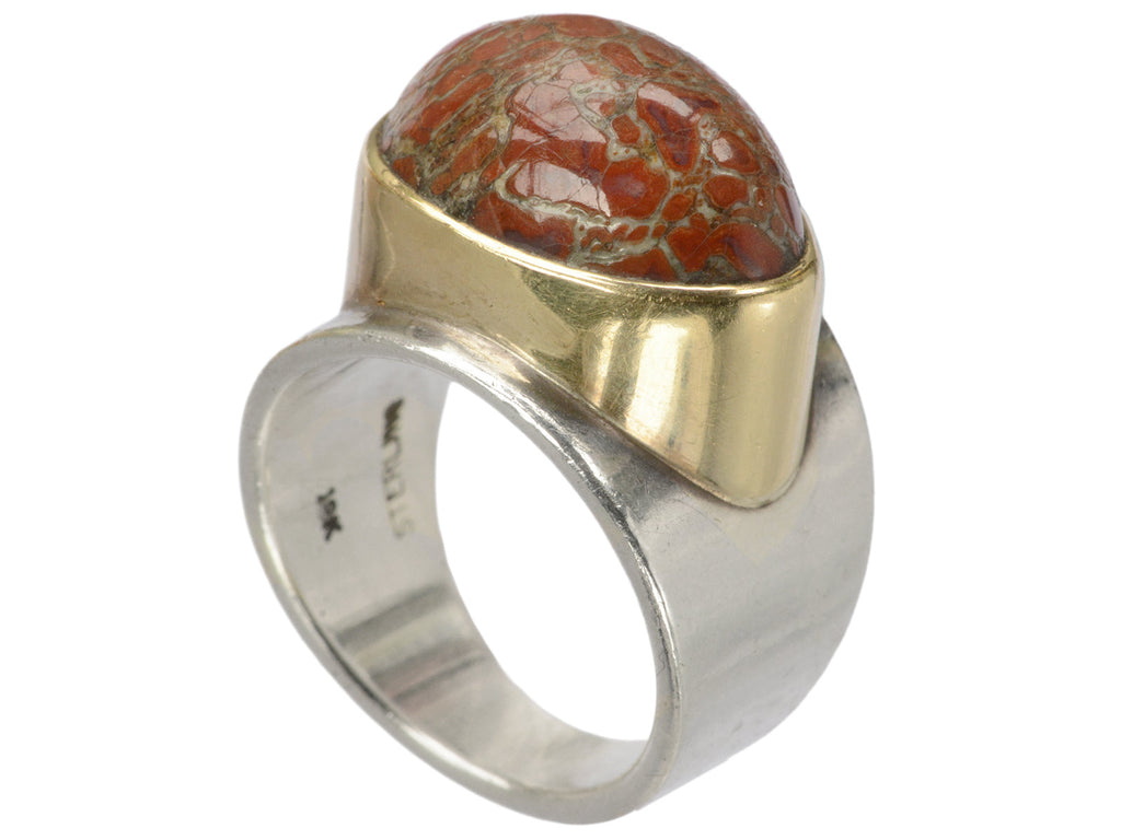 Angled view of fossilized red jasper cabochon set in gold bezel on silver shank, shown on white background.