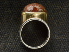 thumbnail of Side profile view of fossilized red jasper cabochon set in gold bezel on silver shank, shown on dark textured background.